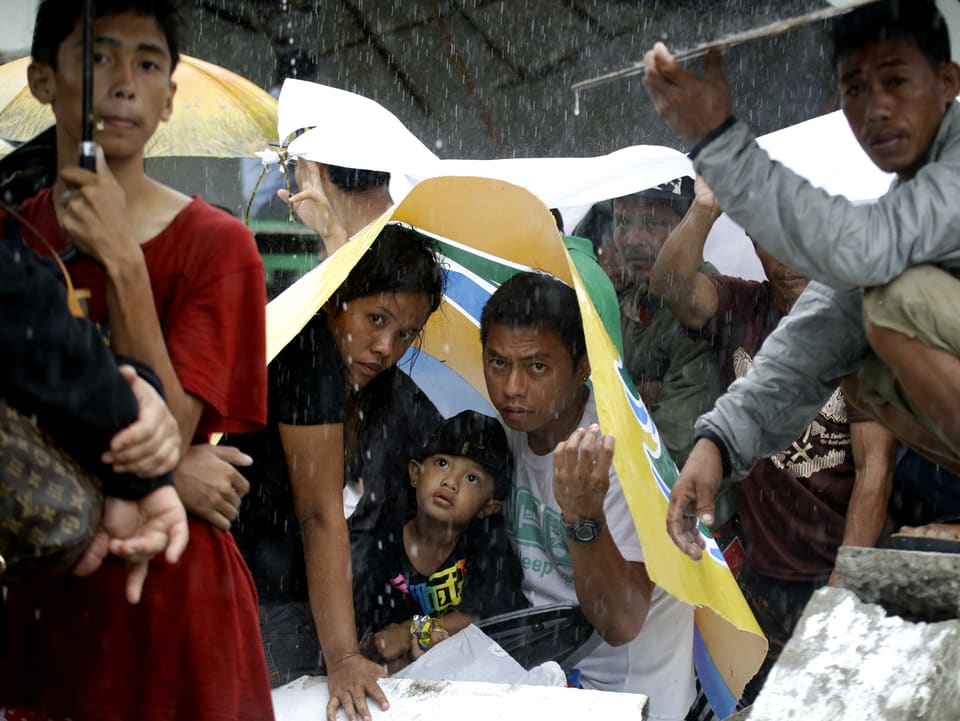 Eine Familie sucht unter einem kleinen Dach Schutz vor dem Regen.