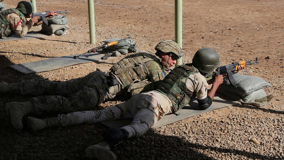 Zwei Soldaten in unterschiedlicher Kampfmontur liegen auf dem Boden, der eine zielt mit einem Gewehr, der andere schaut ihm dabei zu.