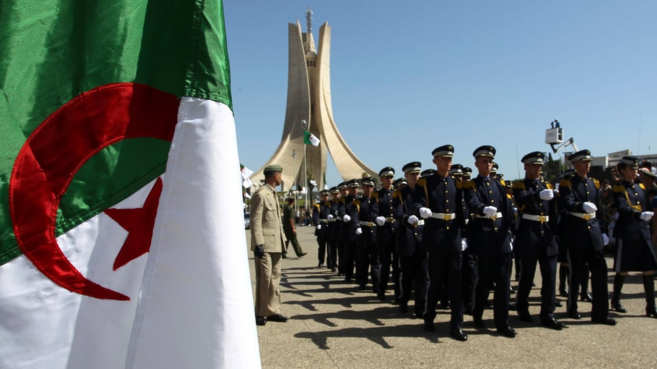 Militärparade mit algerischer Flagge im Vordergrund.