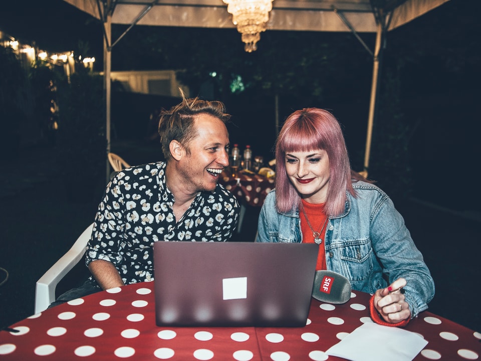 Junge Frau und junger Mann sitzen an einem Tisch und schauen in einen Laptop