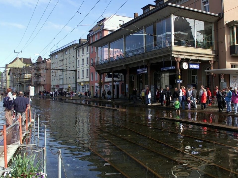 Überflutete Strasse mit Menschen und Geschäften in einer Stadt.