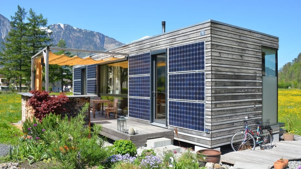 Das Haus mit Terrasse von der Seite. Wo keine Solarzellen sind, sind Holzwände