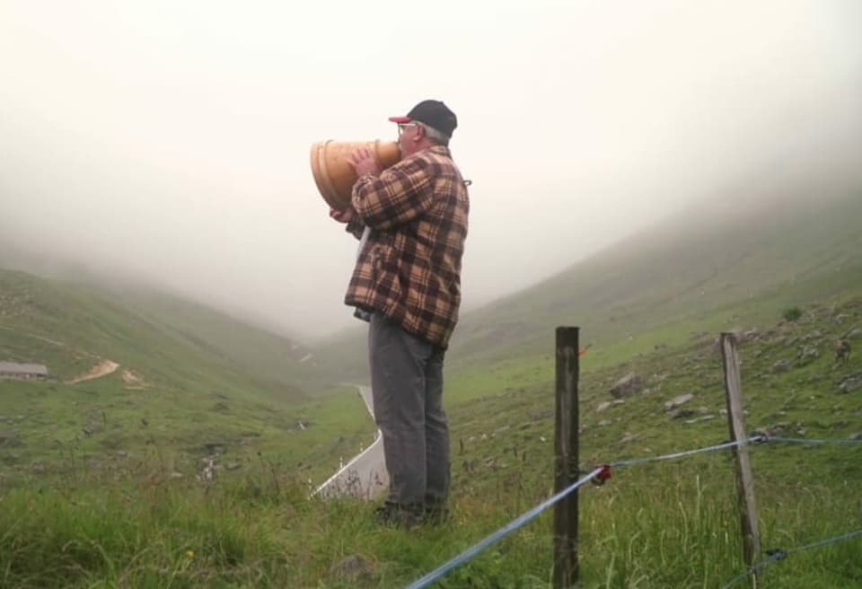 Ein Mann mit einem Milchtrichter in der Hand auf einer Alp.
