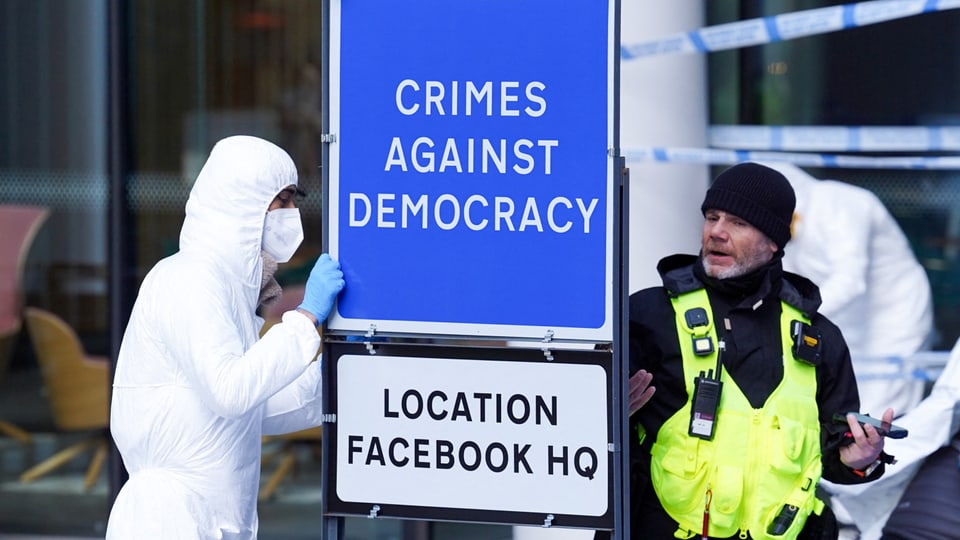 Person in einem weissen Schutzanzug montiert ein Schild «Verbrechen gegen Demokratie».