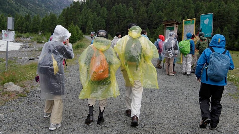 Asiatische Touristen tragen dicke Jacken und Regenschütze bei ihrem Besuch in der Nähe von Pontresina.