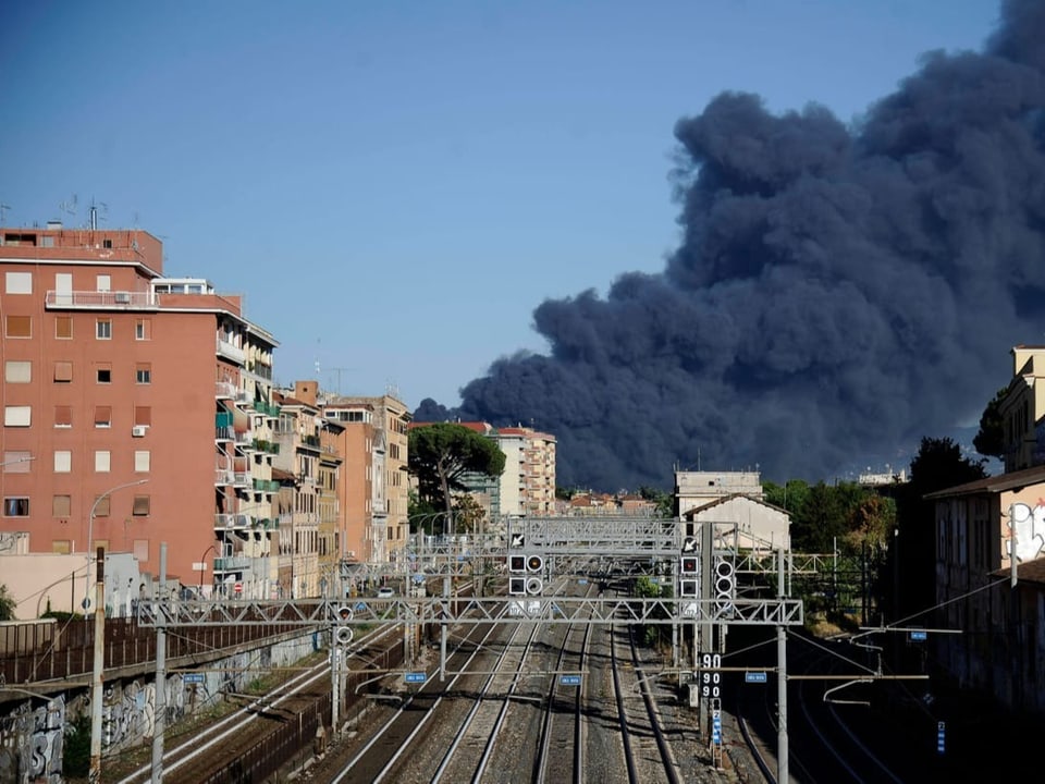 Blick auf ein Gleisfeld in Rom, mit dichter schwarzer Rauchwolke im Hintergrund