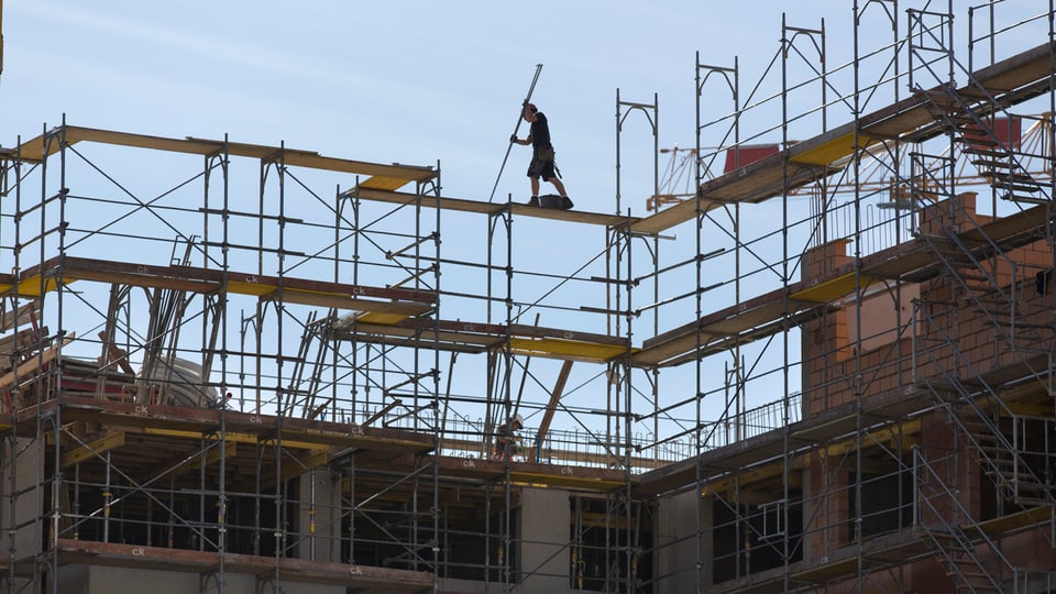 Arbeiter von Ferne zuoberst auf einen Baugerüst auf einer Baustelle im Gegenlicht