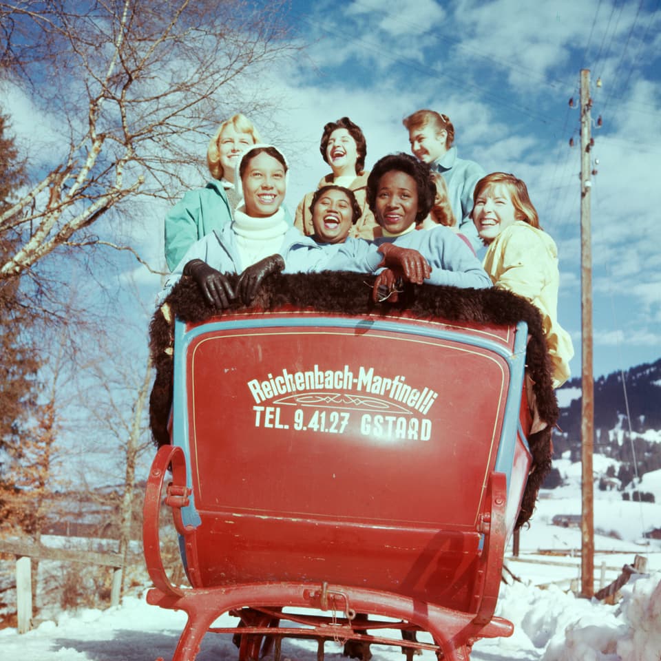 In einem grossen roten Schlitten sitzen lachend junge Frauen verschiedener Hautfarben.