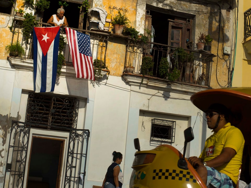 Zu sehen ein Balkon in den Strassen von Kuba. Es hängen zwei Flaggen, die US-amerikanische und die kubanische