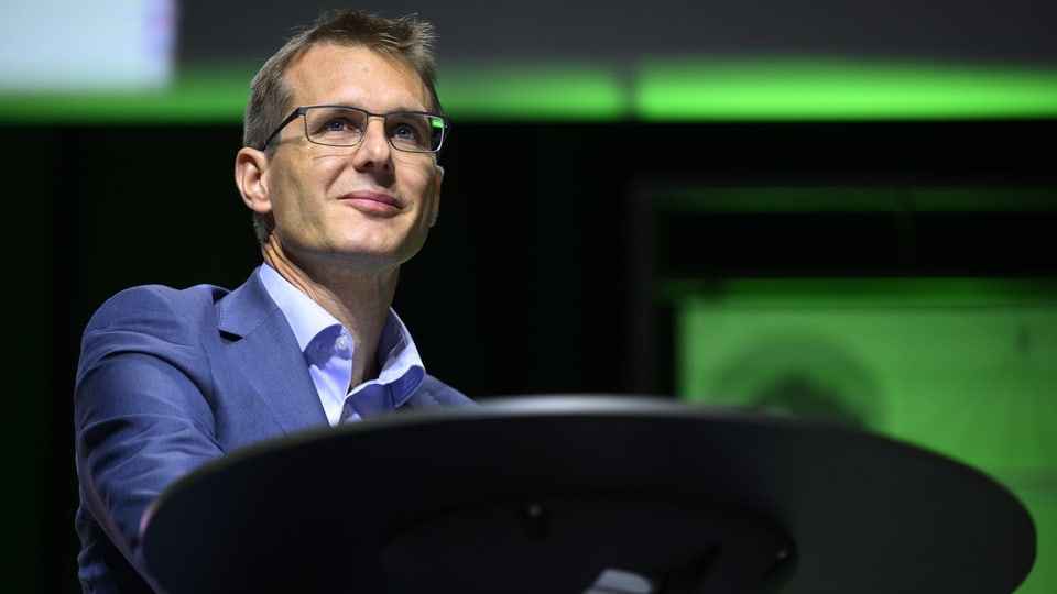 Swisscom-Chef Christoph Aeschlimann steht an einem Hochtisch vor grünem Hintergrund.