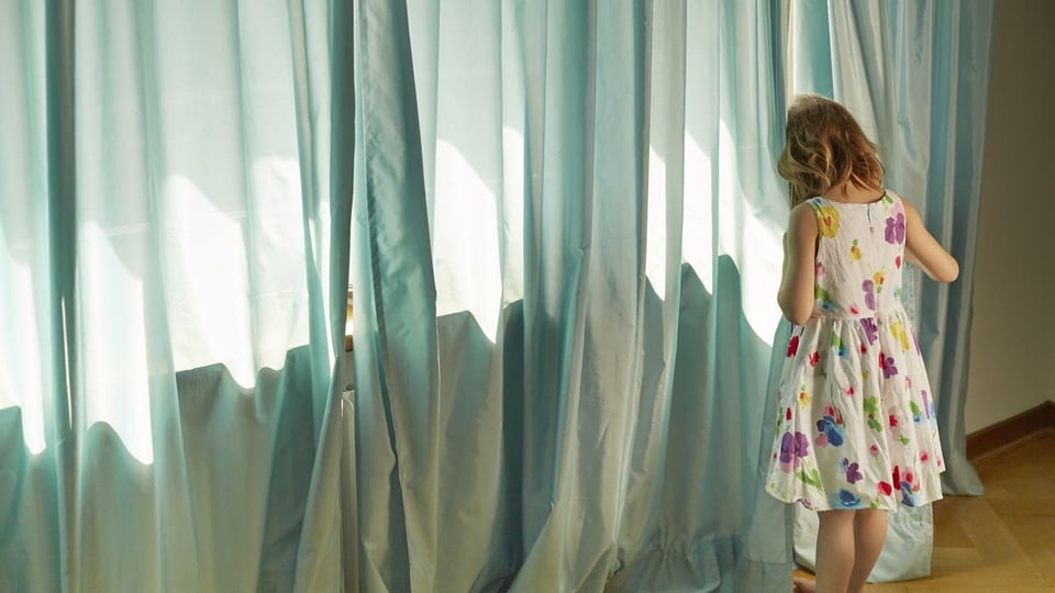 Kleins Mädchen versteckt sich hinter dem Vorhang.
