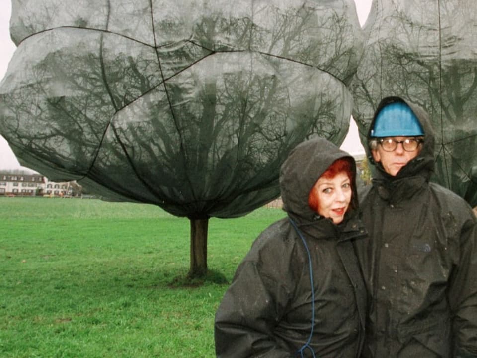 Zwei Leute stehen vor zwei verpackten Bäumen.