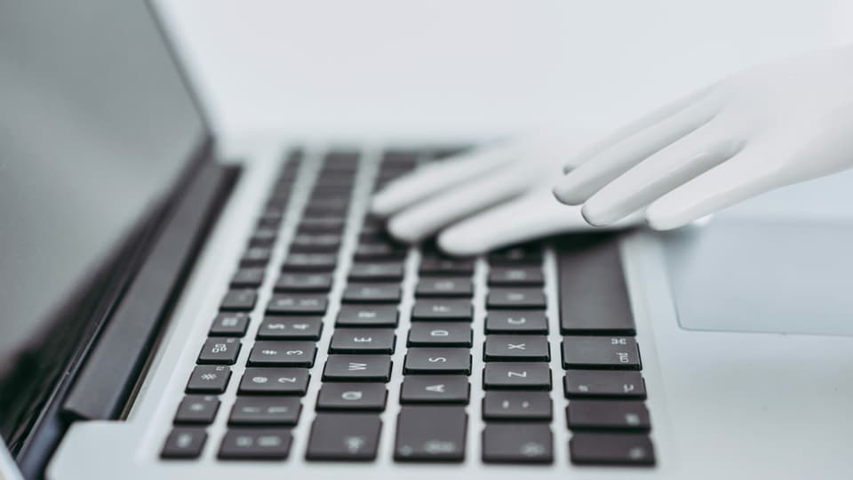 Eine Roboterhand liegt auf dem Keyboard eines Laptops