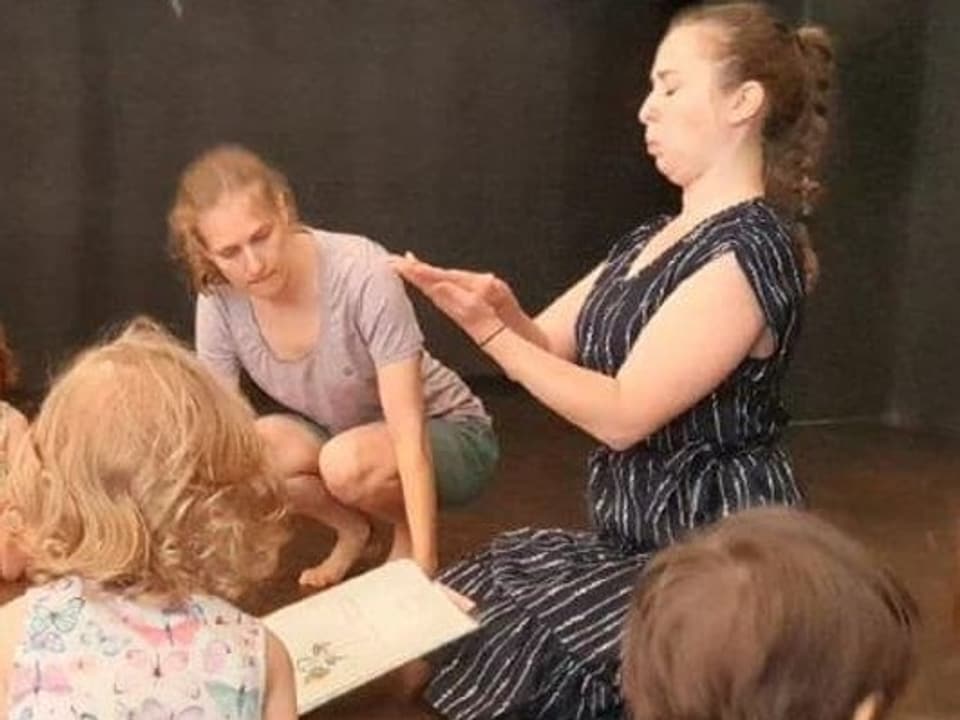 Zwei Theaterschaffende lesen Kindern aus einem Buch vor.