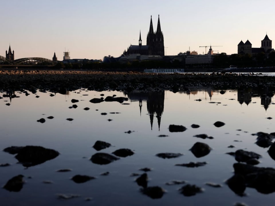 Flaches Wasser aus dem Steine hervorschauen. Dahinter der Kölner Dom.