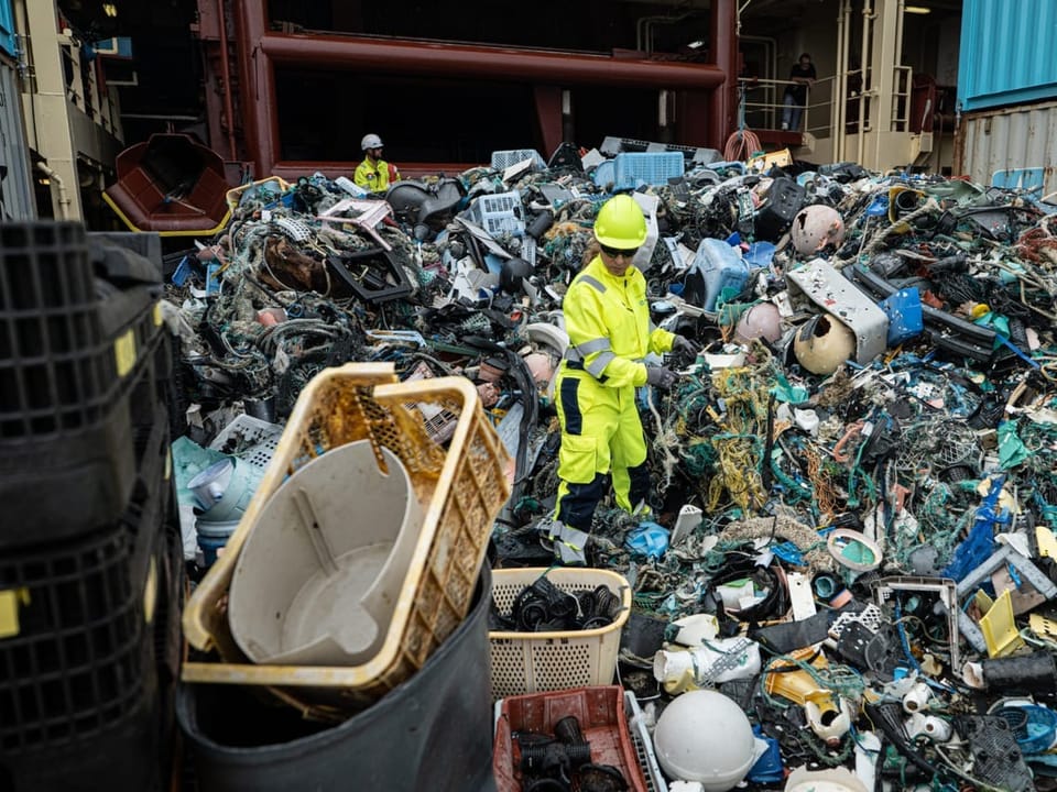 Ein Mann in neongelber Kleidung steht inmitten von Plastikkleidung