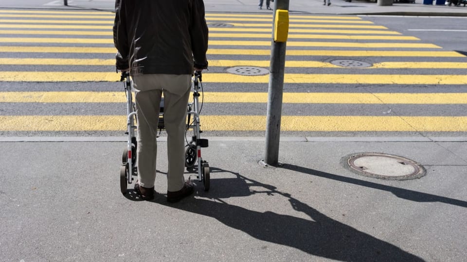 ein älterer Mann steht mit Rollator vor dem Fussgängerstreifen