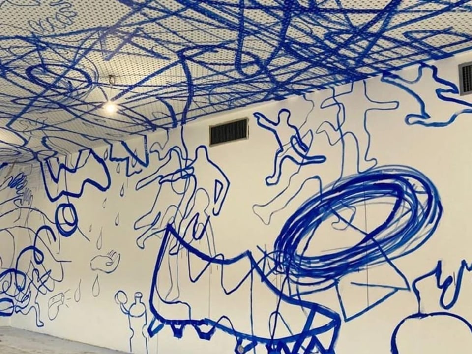 Eine weiss Wand. Darauf sind blaue Linien und kleine Zeichnungen gemalt.