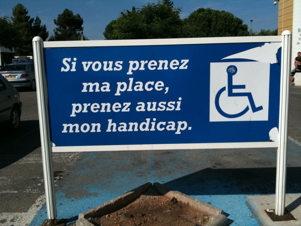 Tafel mit Aufschrift «Si vous prenez ma place, prenez aussi mon handicap.»