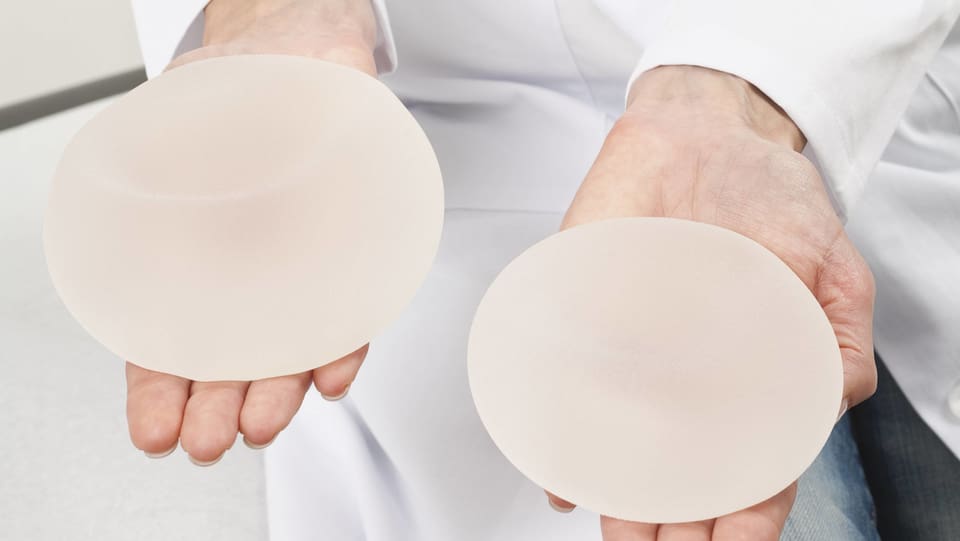Symbolbild: Brustimplantate auf zwei Händen.