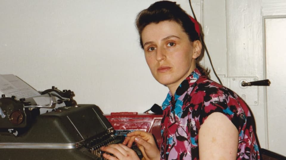 Eine Frau vor der Schreibmaschine blickt in die Kamera.