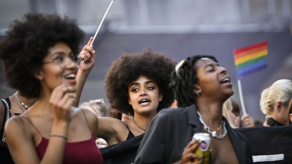 Auf dem Bild sind drei Frauen der Pride Lausanne zu sehen.