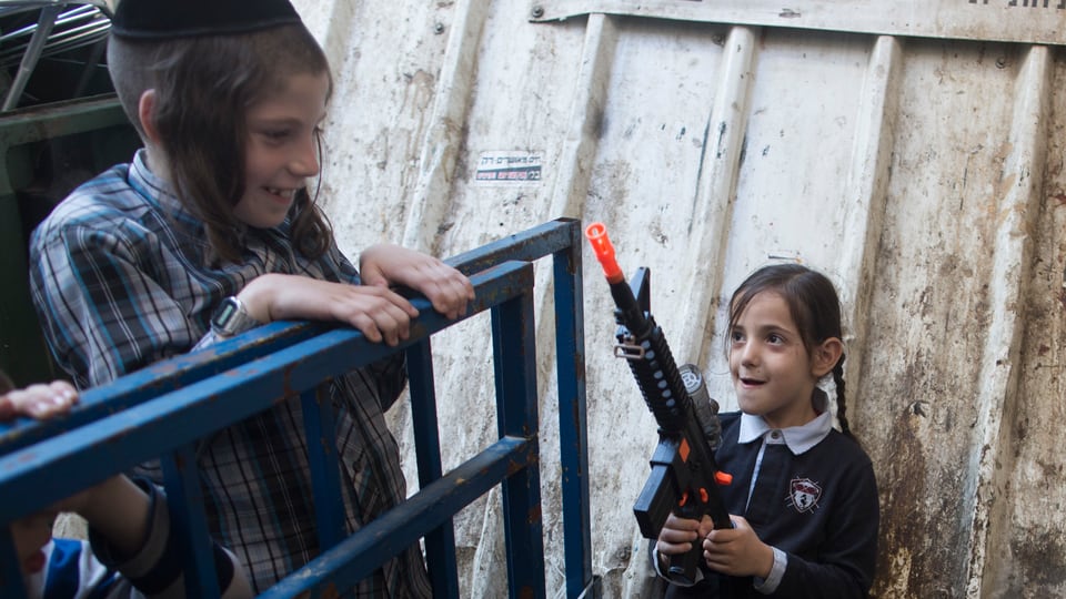 Zwei Kinder spielen, ein Mädchen hält eine Plastikwaffe in der Hand.