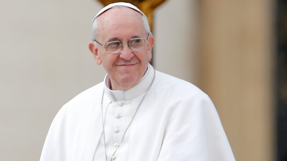 Papst Franziskus vor einem Kreuz mit Blick nach links.