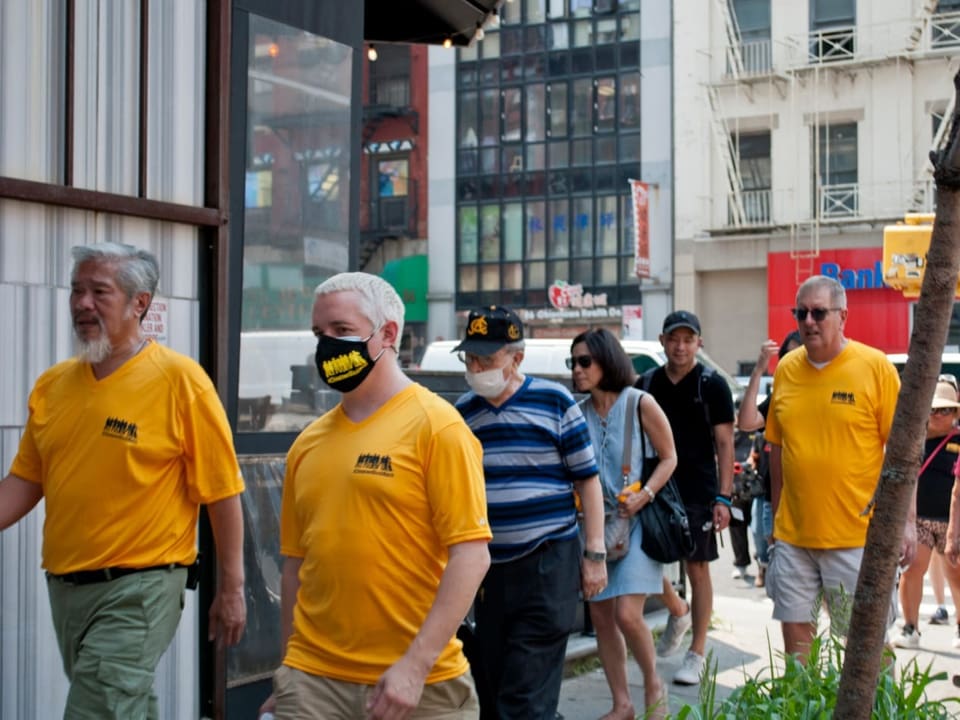 Drei Männer in gelben T-Shirts laufen durch Chinatown in New York