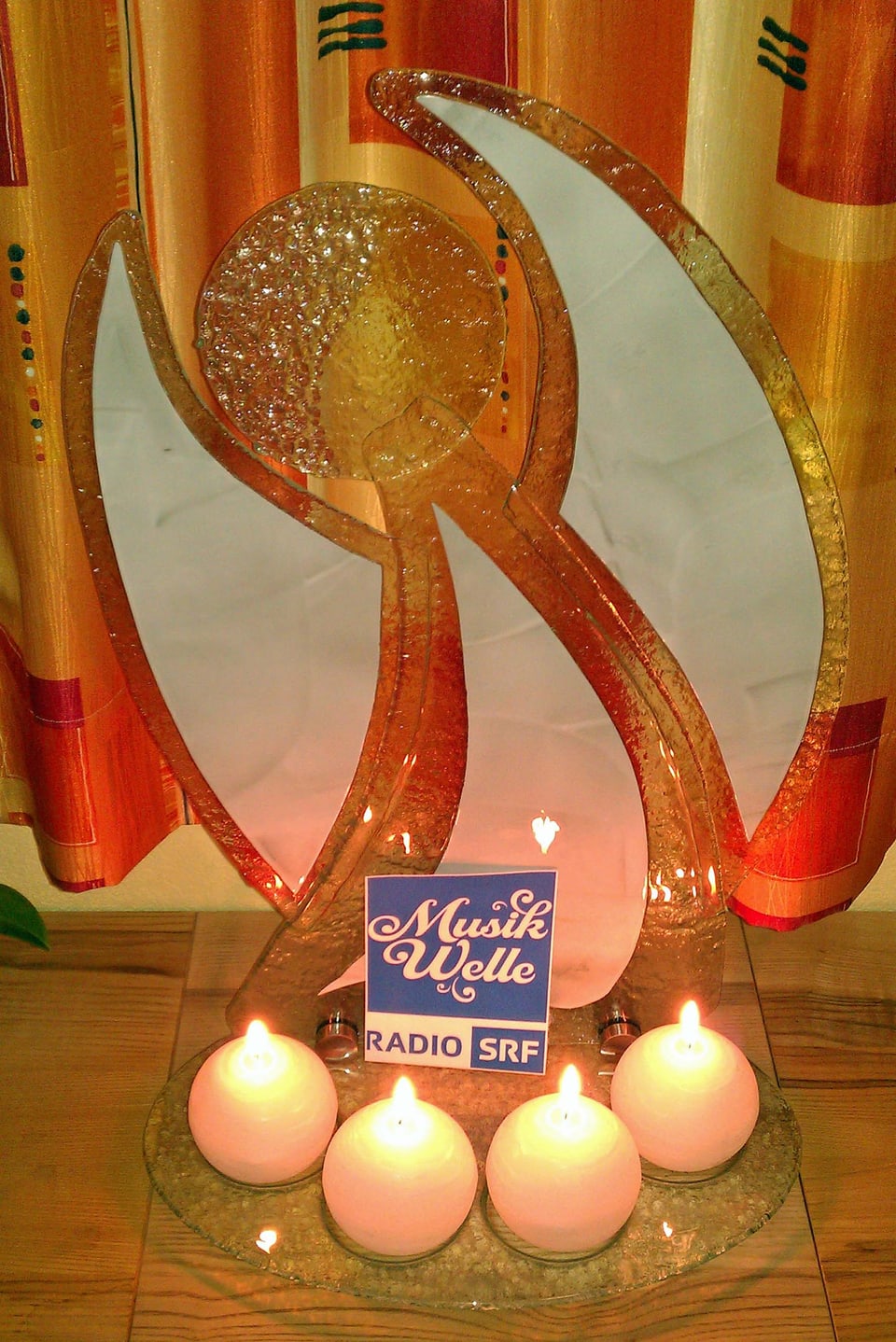 Engel aus Glas mit vier runden Kerzen und dem Logo von SRF Musikwelle
