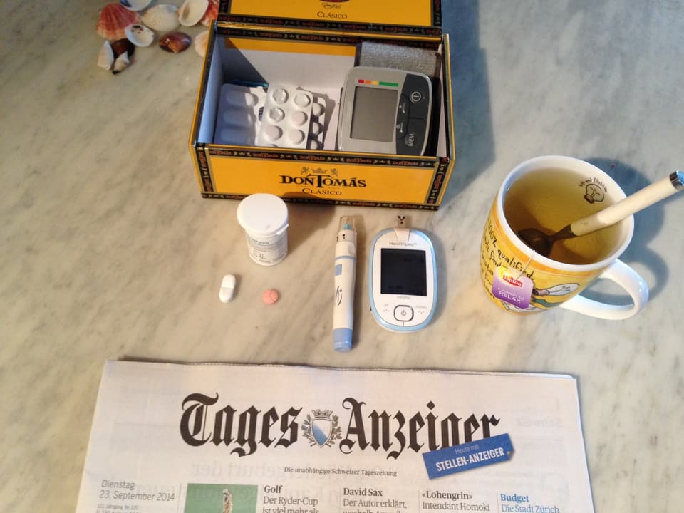 Zeitung, Tee und Medikamente auf dem Tisch.