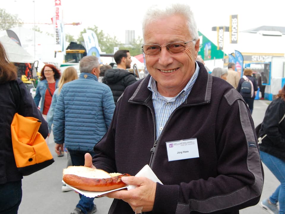 Mann hält einen Pappteller mit einer Bratwurst in der Hand. 