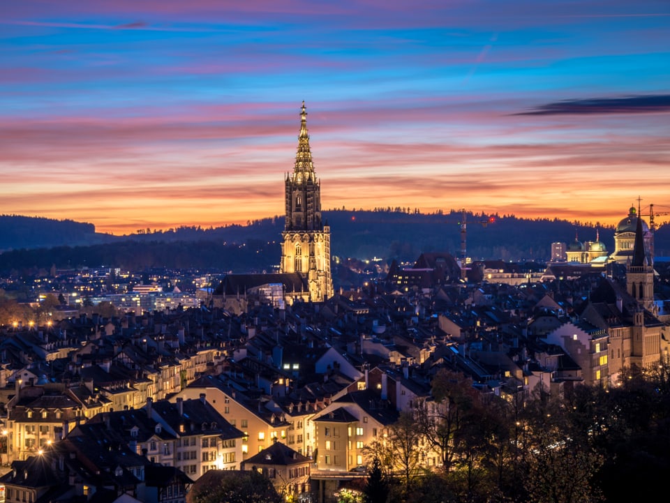 Der Himmel hinter dem Berner Münster steht in den Farben Dunkelblau, Rot und Gold.