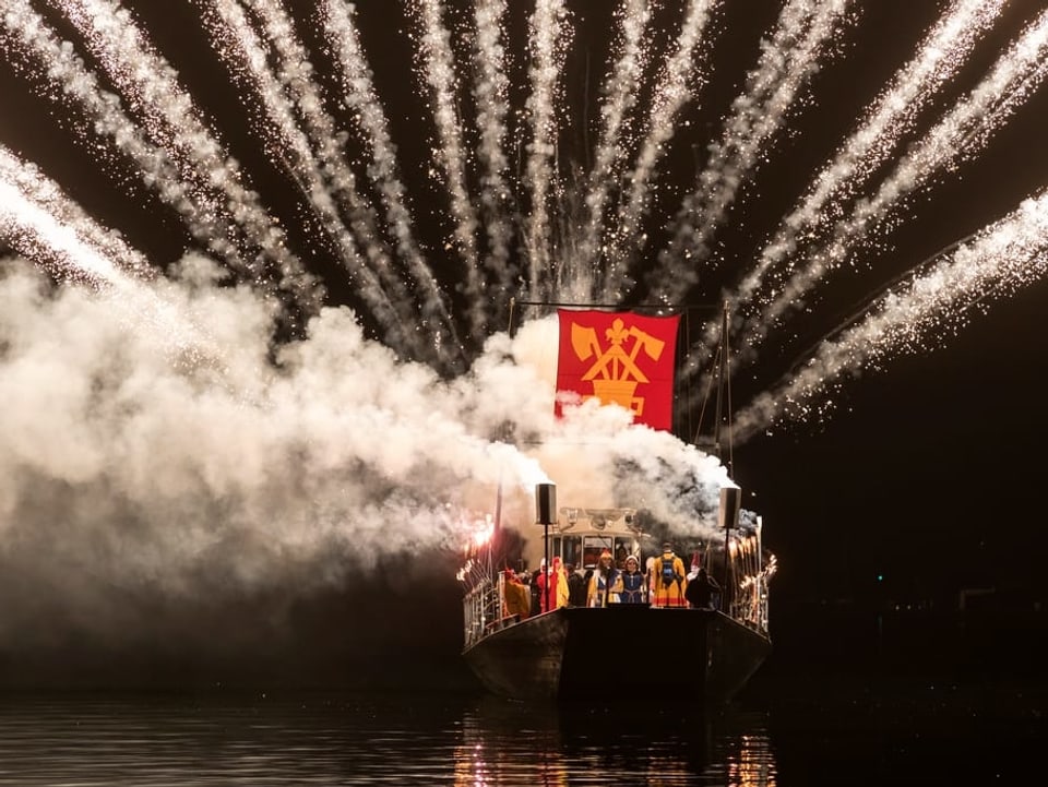 Ein Nauen mit Fasnächtlern an Bord und der Fahne der Safranzunft gehisst. Eine Rauchbombe hüllt das Schiff in Rauch. 