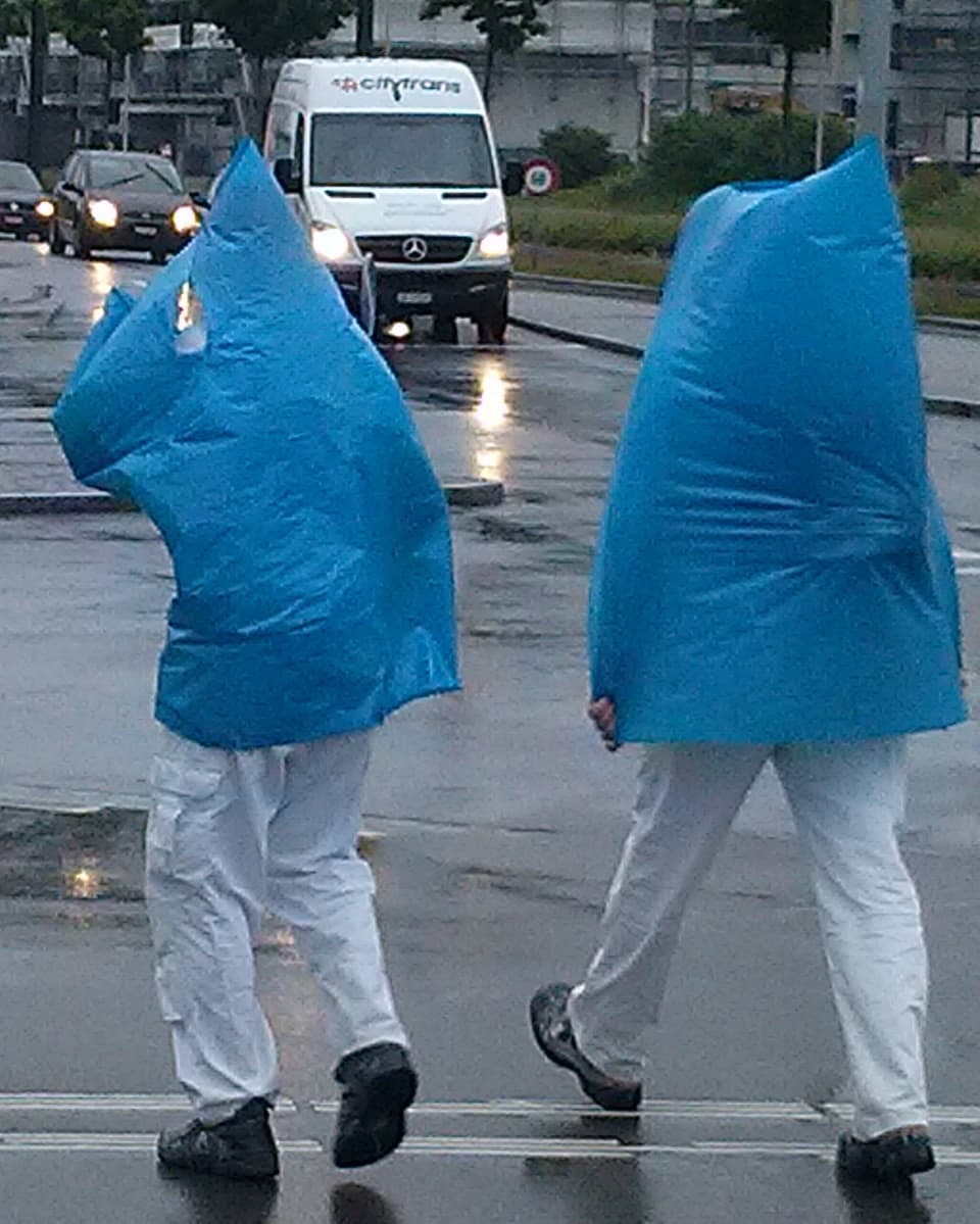 Zwei Personen mit übergestülpten blauen Müllsäcken spazieren durch den Regen.
