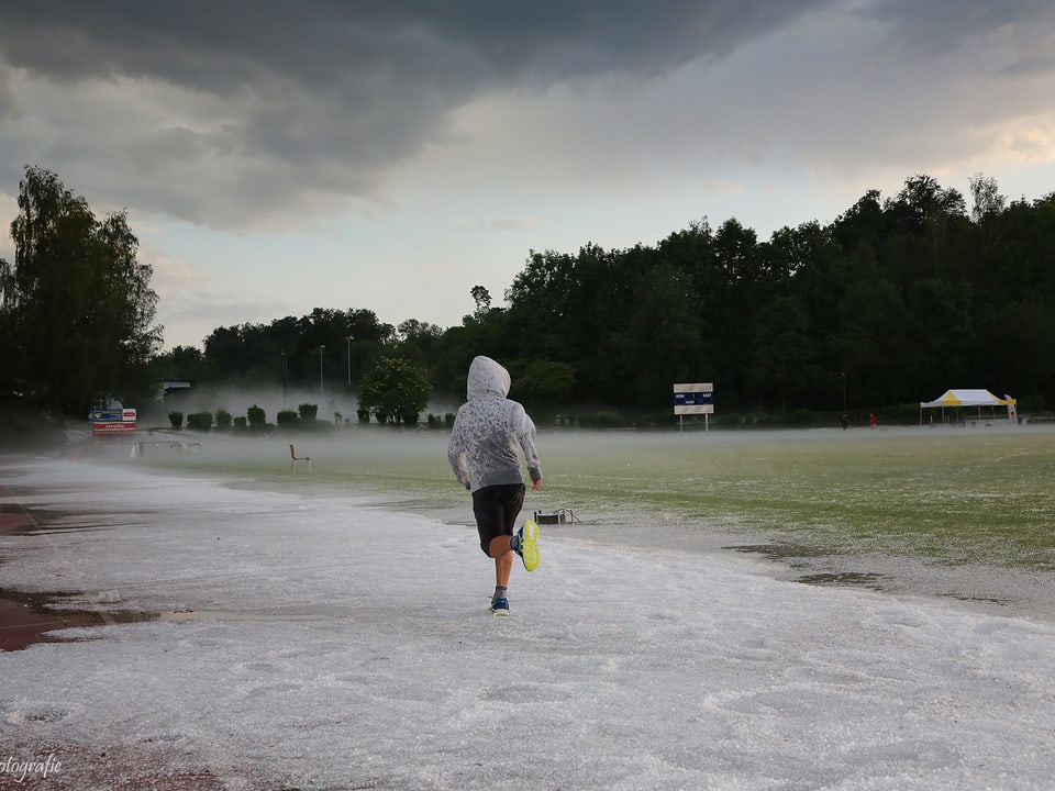 Ein Jogger läuft bei  Hageauf einer Sportanlage, seine helle Regenjacke schützt ihn nur wenig.