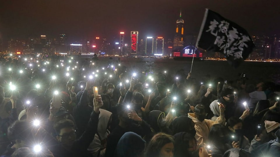 Eine Menschenmenge zündet kleine Lichter an am Flussufer in Hongkong.