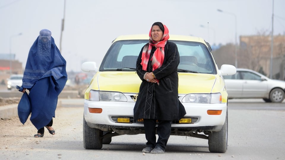 Symbolbild: zwei Frauen in Afghanistan, eine in einem Ganzkörperschleier, die andere lehnt mit Kopftuch an ein Auto.