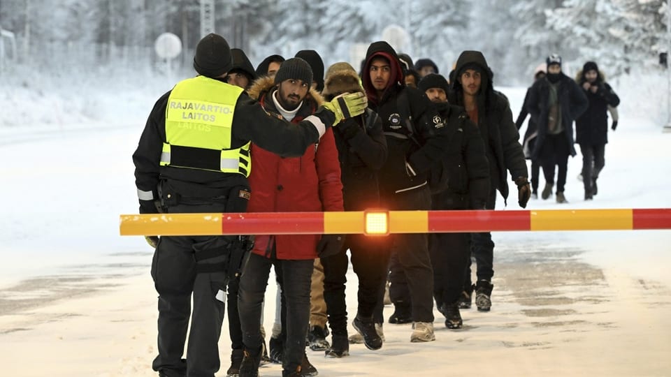 Menschen aus dem Nahen Osten in Turnschuhen, die vor einer Grenzbarriere stehen im Schnee