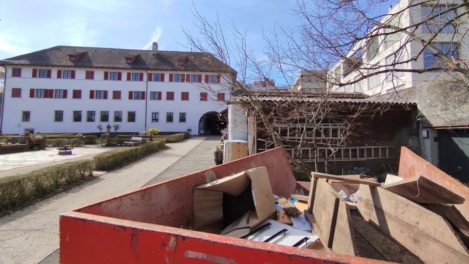 Renovierungsarbeiten mit Container und Baumaterialien vor einem historischen Gebäude.