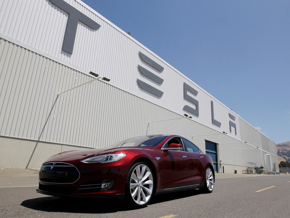 Tesla Model S in weinrot vor einem Tesla-Gebäude.