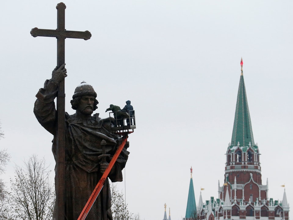 Statue in Halbtotale, zwei Leute arbeiten an der Statue, im Hintergrund der Kreml.