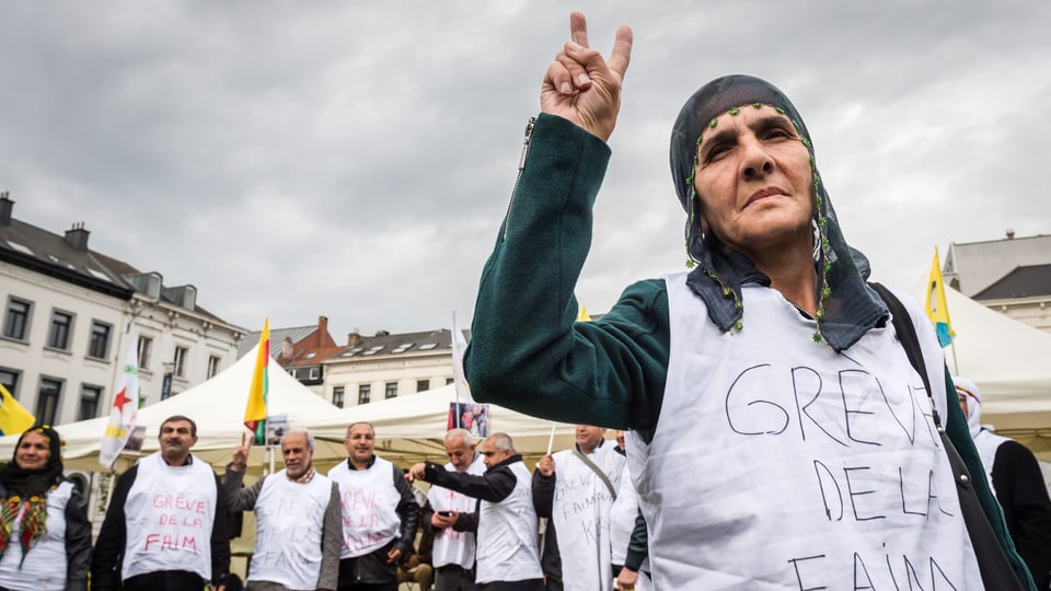 Im Vordergrund eine ältere Frau, sie macht ein Victory-Zeichen und trägt ein Shirt, auf dem steht «grève de faim», hinter ihr weitere Frauen und Männer mit gleichen Shirts.