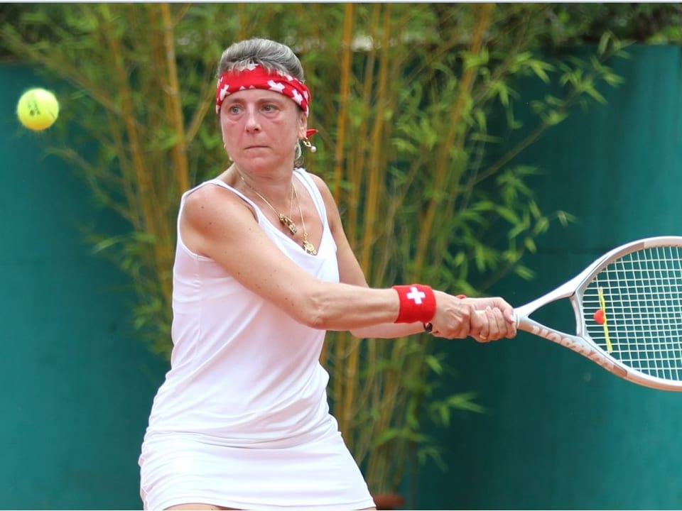 Frau spielt Tennis und schaut konzenriert auf den Ball in der Luft gleich vor ihr.