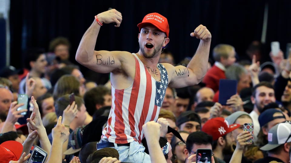 Mann sitzt auf anderem und hat «build the wall» auf seine Ärme geschrieben