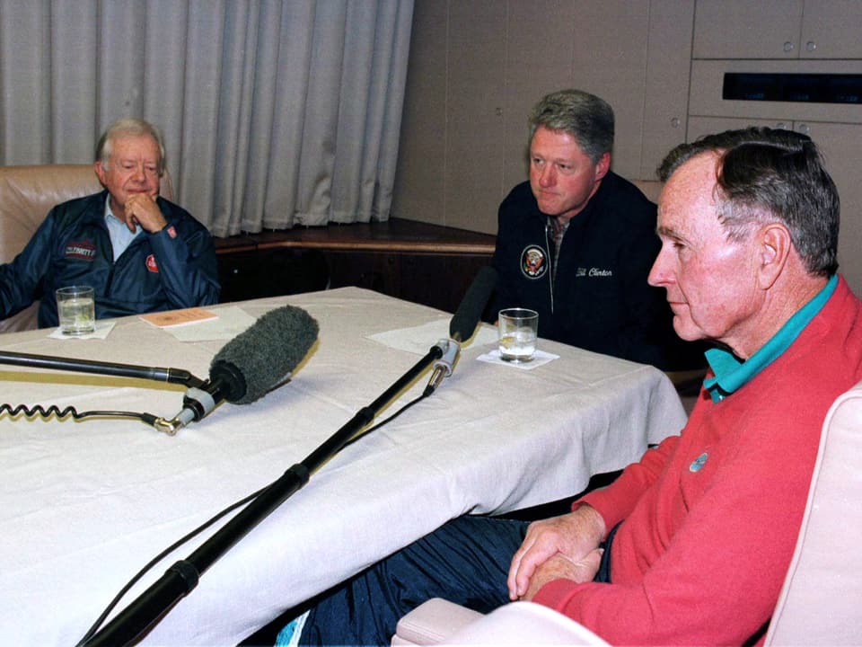 George Bush (rechts), Bill Clinton (Mitte) und Jimmy Carter (links) sitzen an einem Tisch in der «Air Force One» 