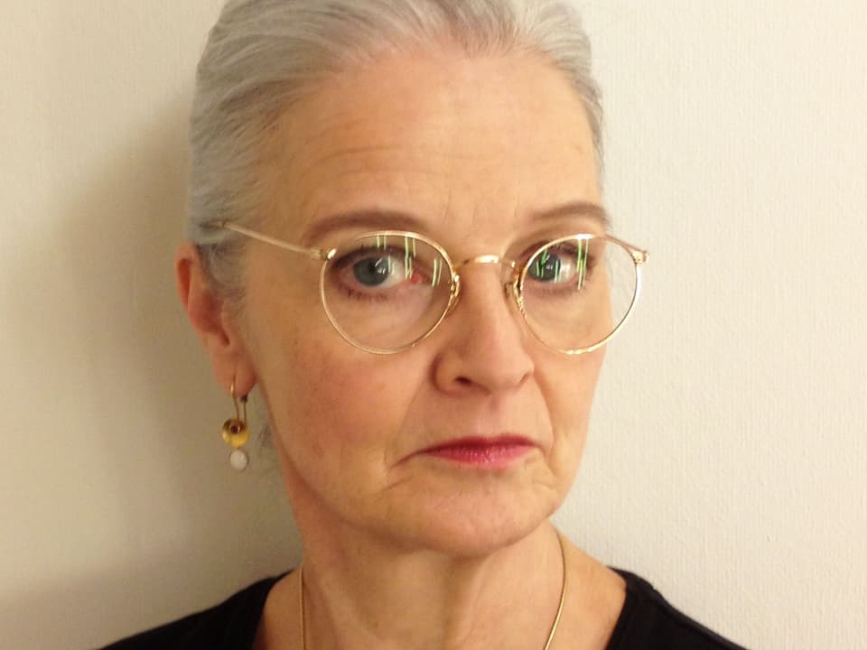 Eine Frau mit grauem Haar und einen runden, goldenen Brille.