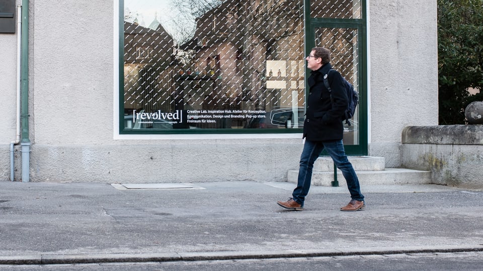 Ein Mann geht auf einem Trottoir an einem Schaufenster vorbei.