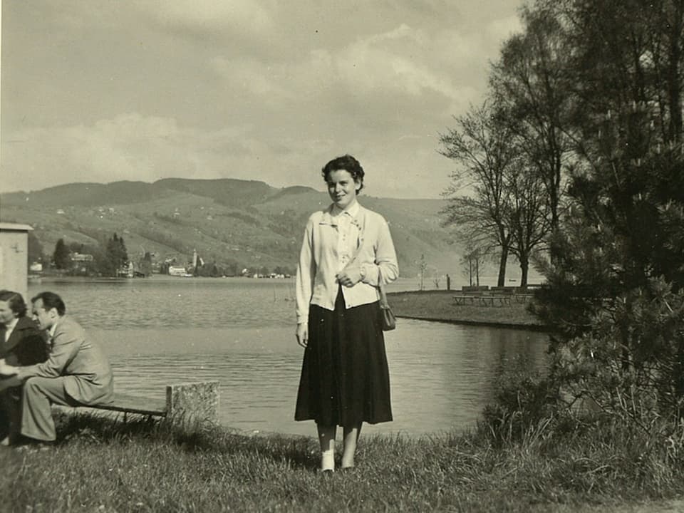 Eine junge Frau steht am Ufer eines Sees.