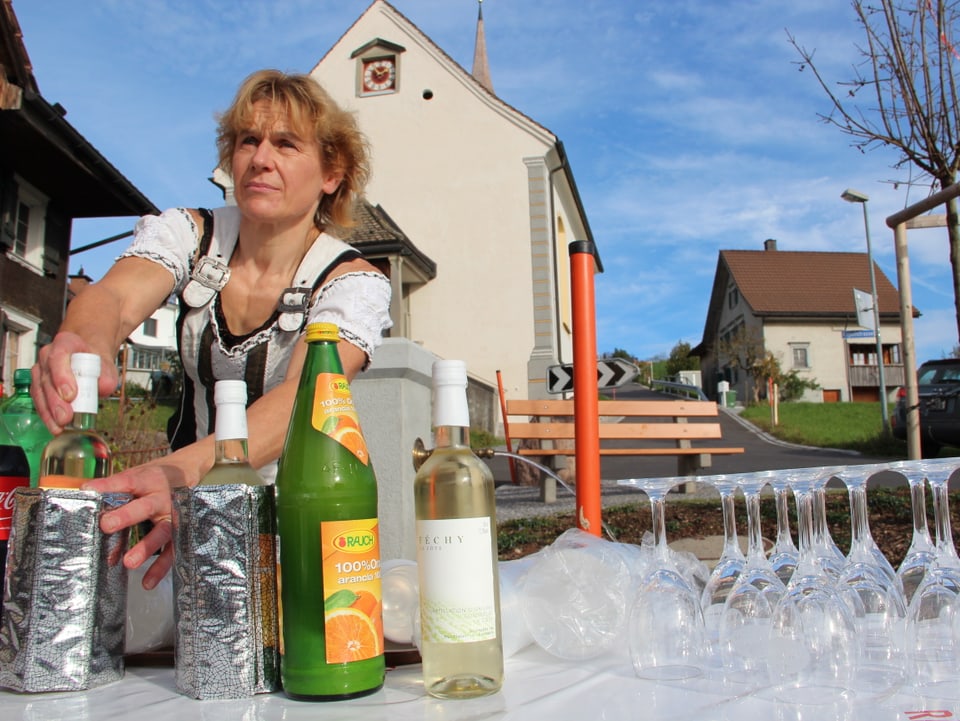 Eine Frau stellt auf einem Tisch im Freien eine Flasche Weisswein in einen Kühlbehälter.